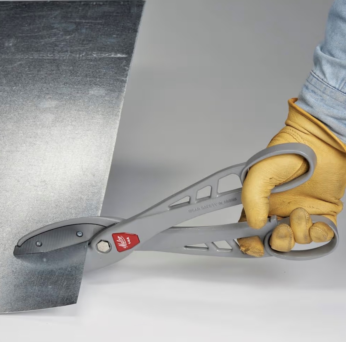 Malco straight snips cutting sheet metal, held in a yellow work glove